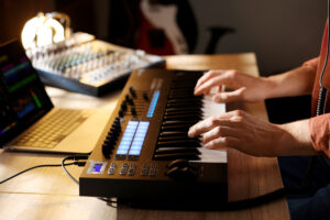 man working with midi keyboard at wooden table indoors, closeup